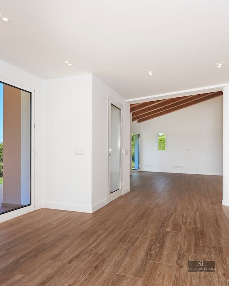 Large empty living room with wood floors, white walls, and sliding glass doors opening to a green garden.