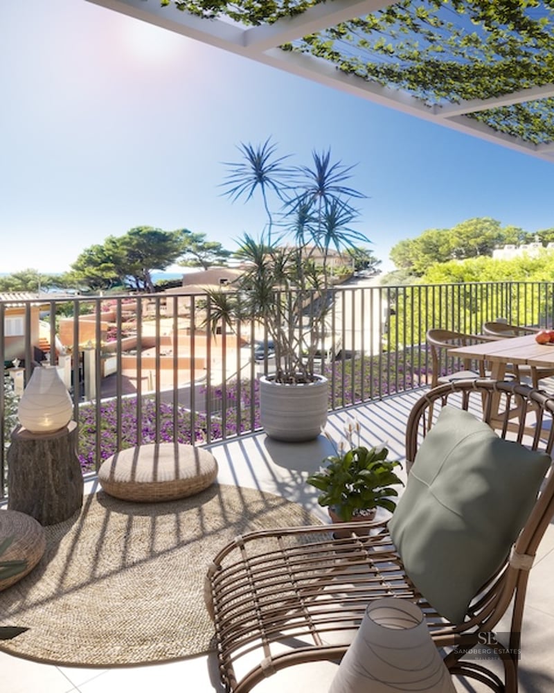 Sunny terrace with wooden dining table, rattan lounge chair, and vine-covered pergola overlooking the sea.