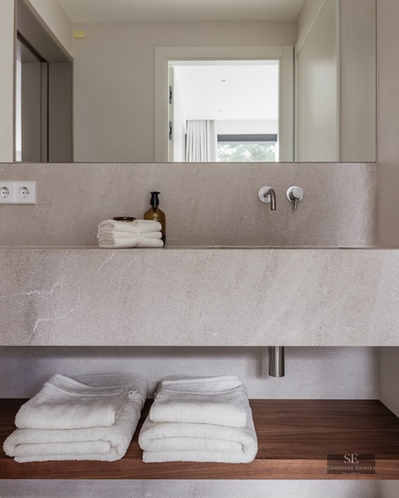 Close-up of a floating stone bathroom sink with a wooden shelf below and folded white towels.
