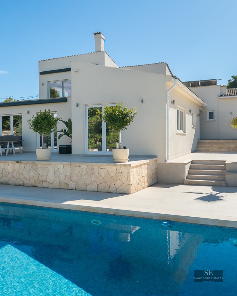 Piscine turquoise devant une villa blanche moderne avec terrasse en pierre sous un ciel bleu clair.