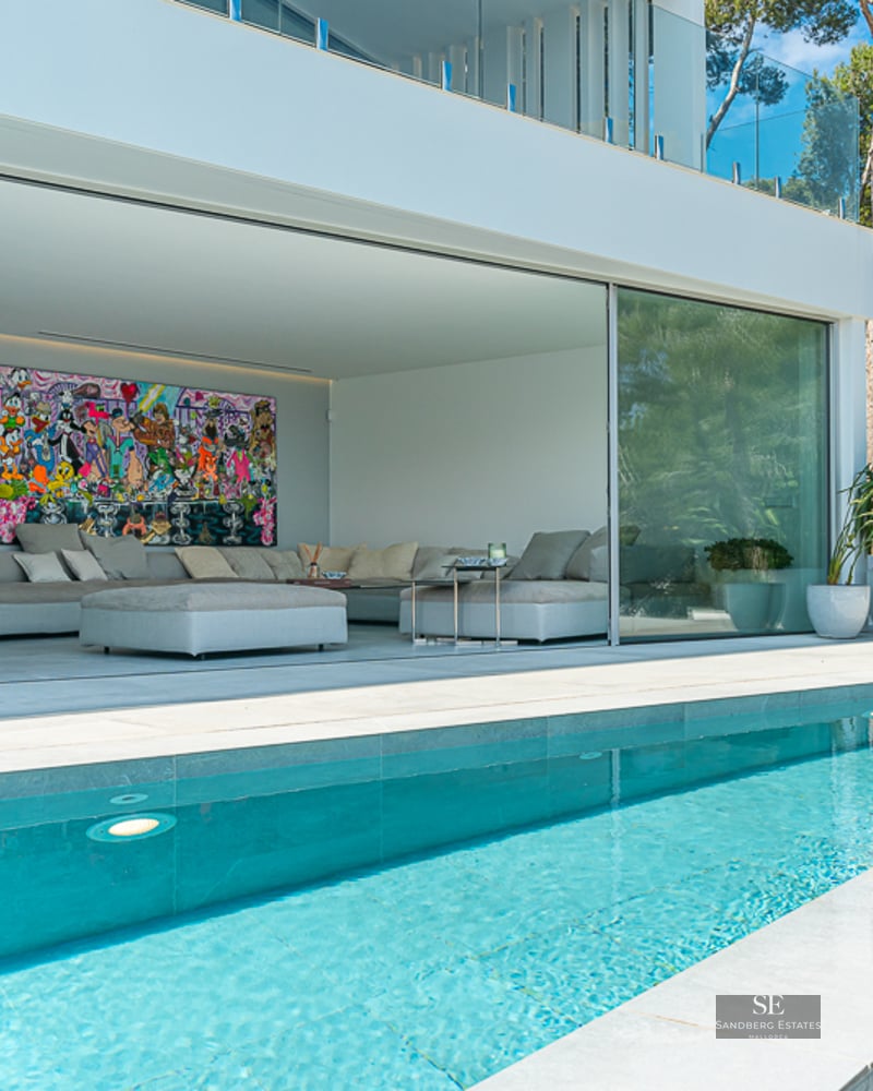 A crystal-clear pool in front of a modern open-plan living room with large glass sliding doors and pop art.