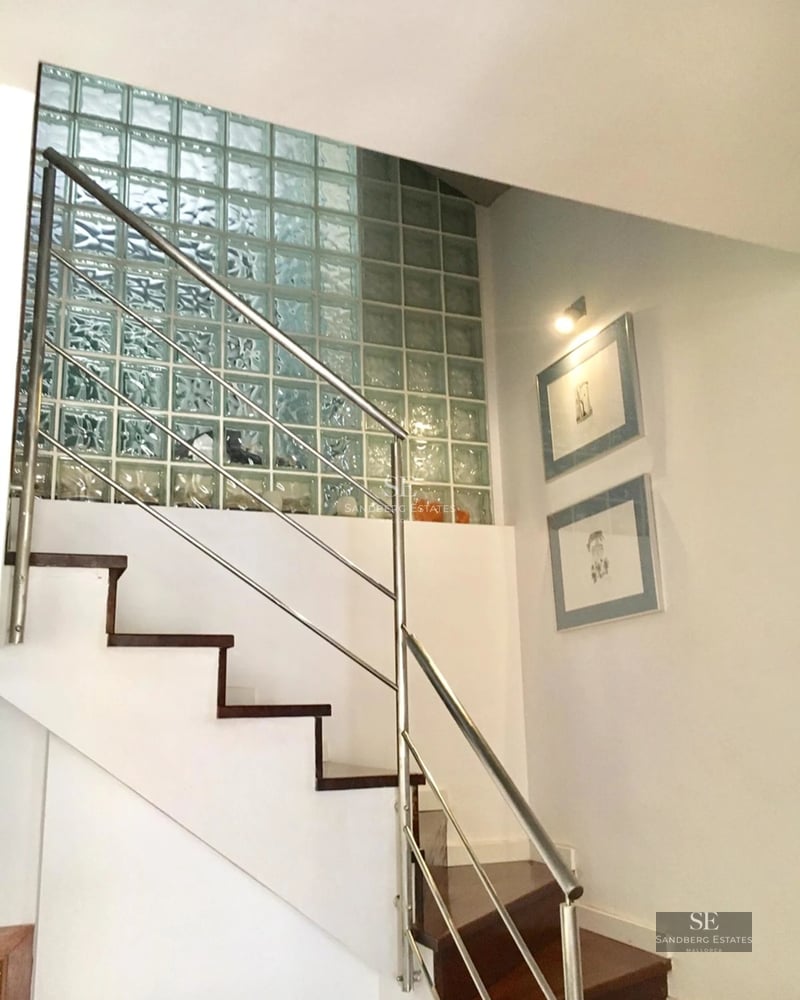 Wide view of a swimming pool with lounge chairs and umbrellas. Modern and minimalist architecture. Green lawn and blue sky.