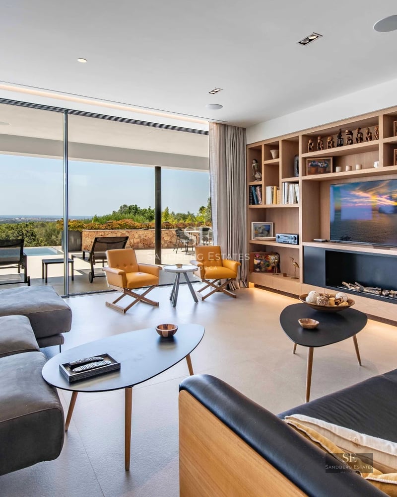 View of infinity pool surrounded by wooden deck with modern furniture. Minimalist architecture with large windows.