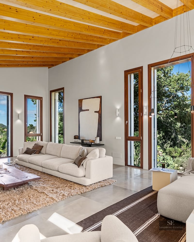 Spacious modern living room with wooden beamed ceilings, white sofas, and large windows looking out to mountains.