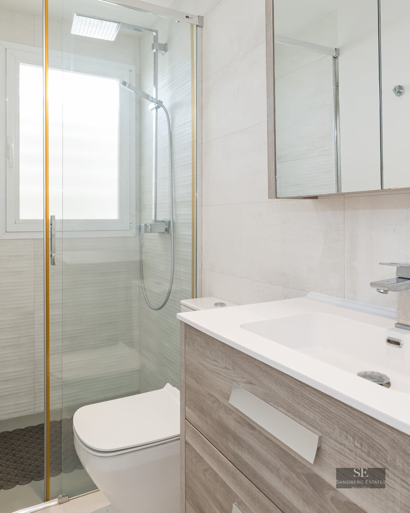 Bright bathroom featuring a wooden vanity, large mirror, and glass walk-in shower.