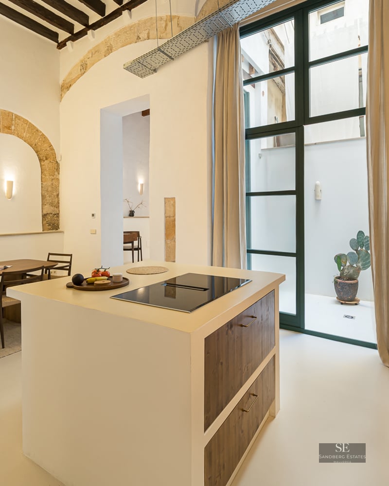 Modern kitchen island and dining table under high ceilings with exposed stone arches and large paper lanterns.