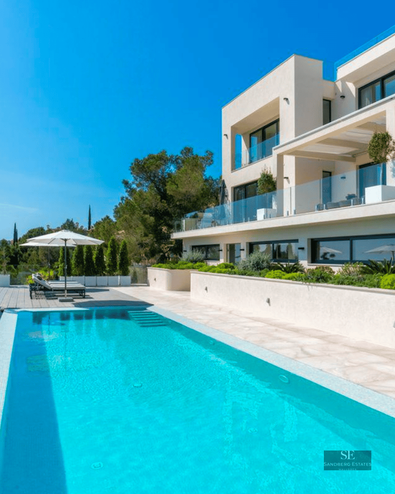 Modern white villa with a turquoise infinity pool overlooking the sea under a clear sky.