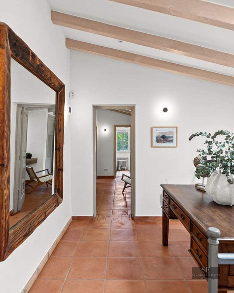 Hallway with orange tile floor, large wooden mirror, antique desk, and exposed ceiling beams.