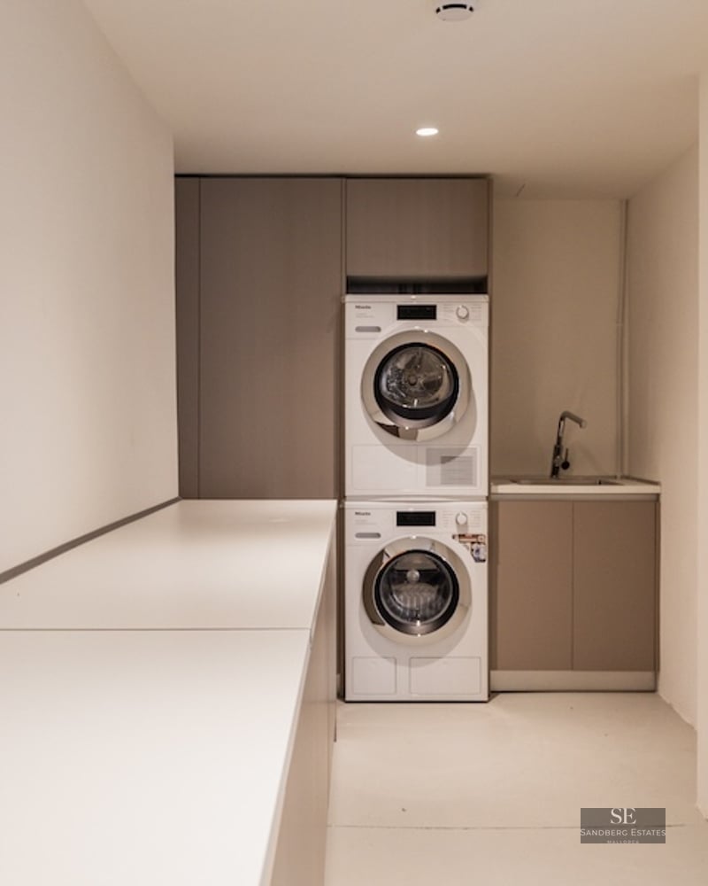 Stacked Miele washer and dryer in a minimalist laundry room with beige cabinetry and a long white countertop.