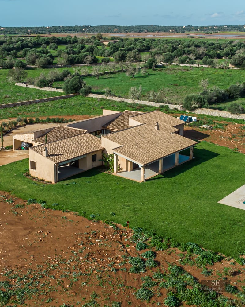 Bird's eye view of a sand-colored modern villa with a turquoise pool and large lawn in a rural landscape.