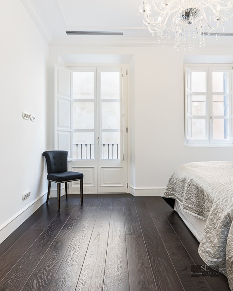 Master bedroom featuring dark wood floors, crystal chandelier, and a view into a marble bathroom with a bathtub.