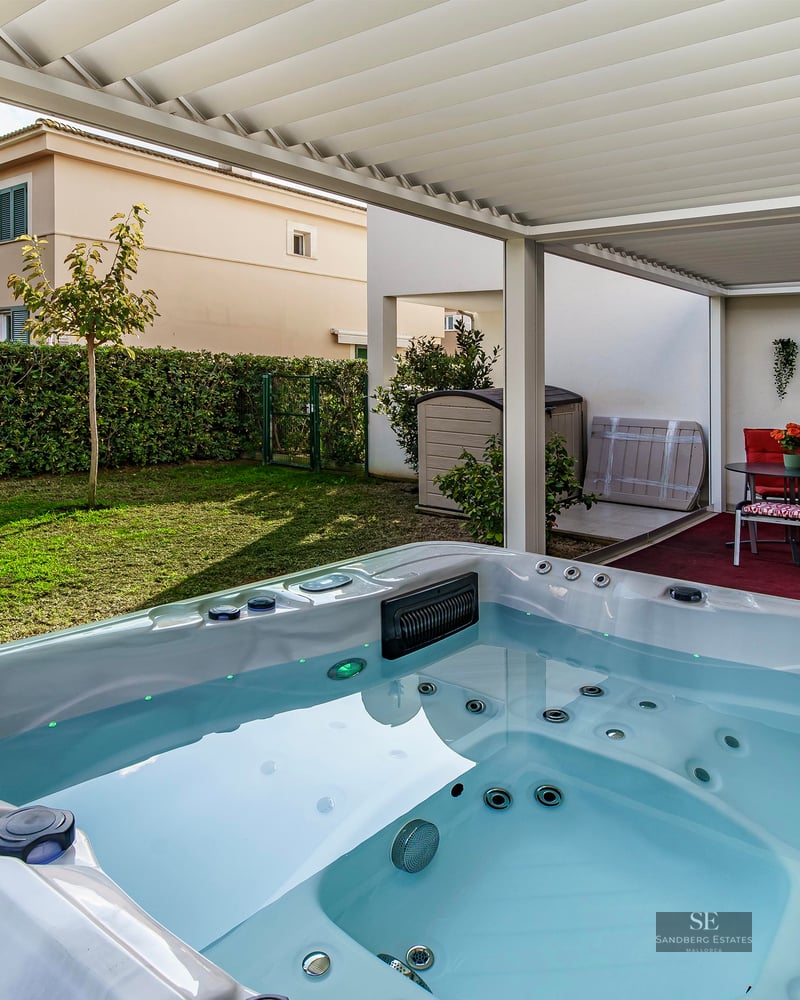 White luxury hot tub under a slatted pergola overlooking a private green garden and outdoor seating area.
