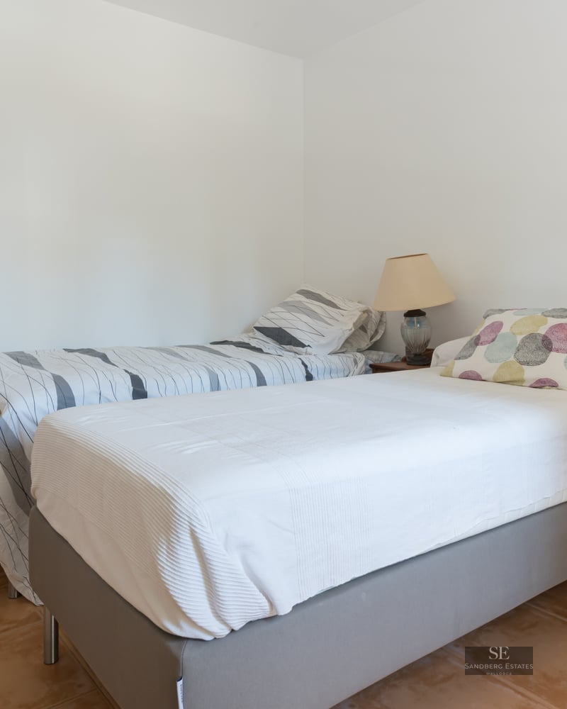 Simple bedroom featuring two single beds, terracotta tile flooring, and clean white walls.