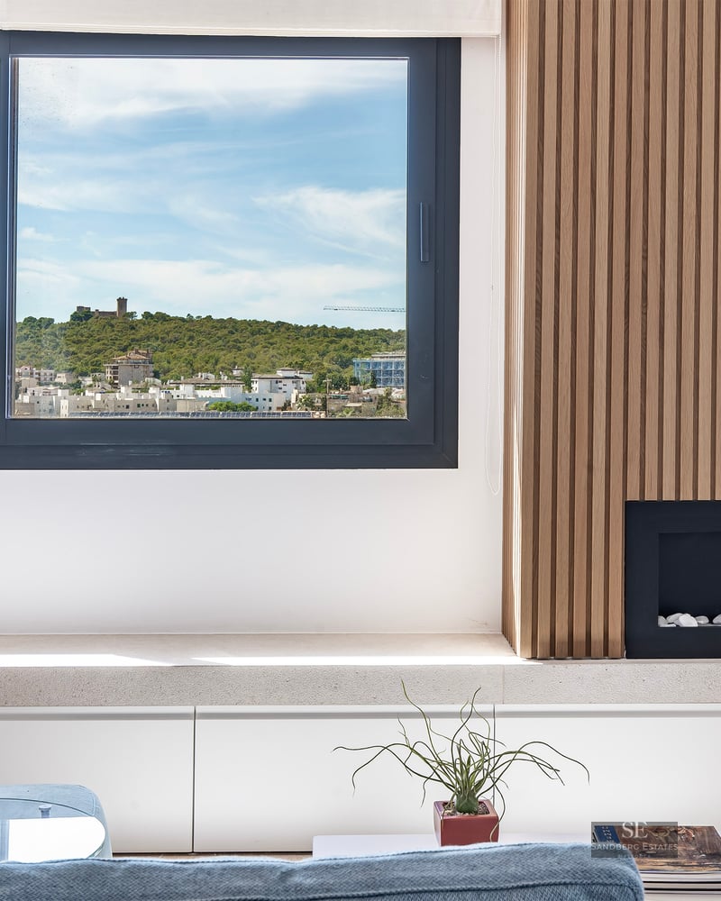 Modern living room with slatted wood wall, built-in fireplace, and a large window overlooking a hilltop castle.