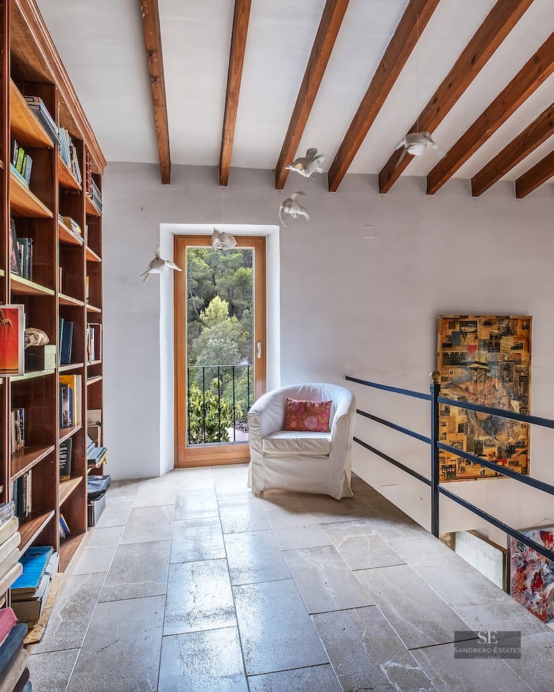 Mezzanine library featuring floor-to-ceiling wooden bookshelves, stone flooring, and rustic exposed ceiling beams.