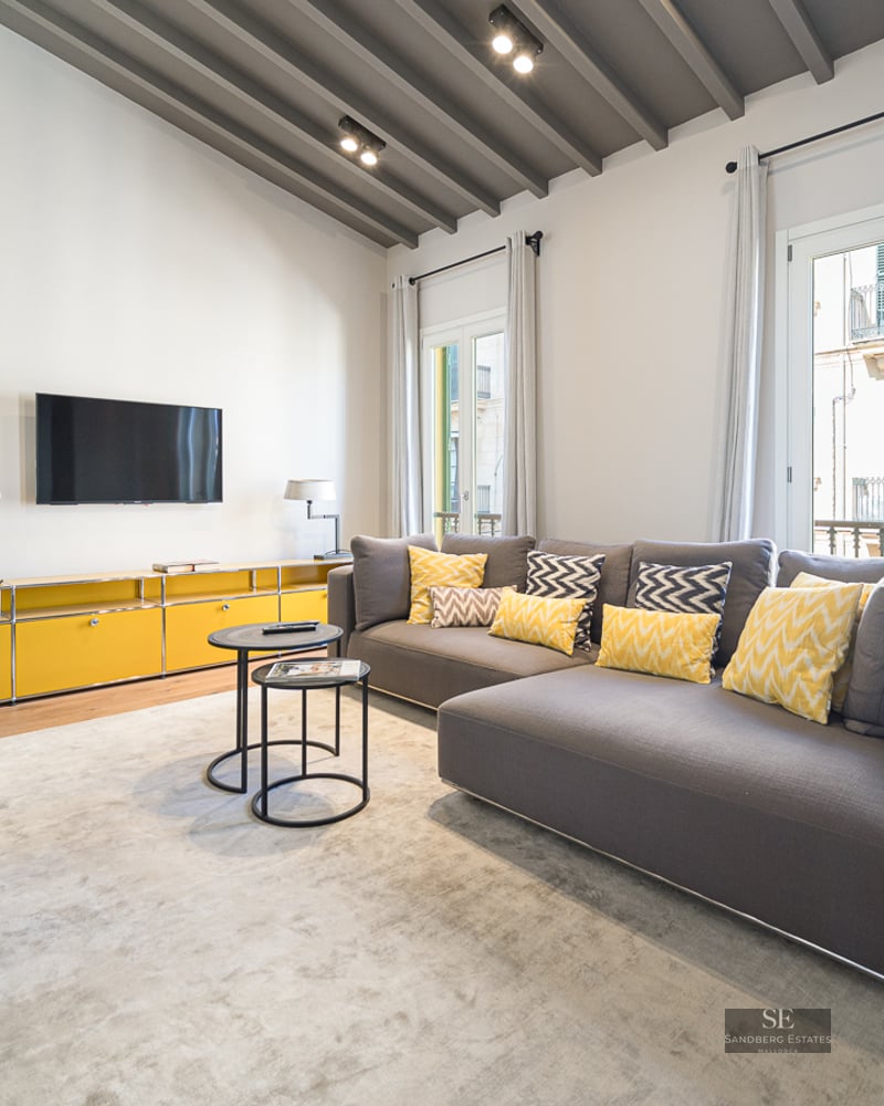 Modern living room featuring a grey sectional sofa with yellow cushions, vaulted beamed ceiling, and a fireplace.