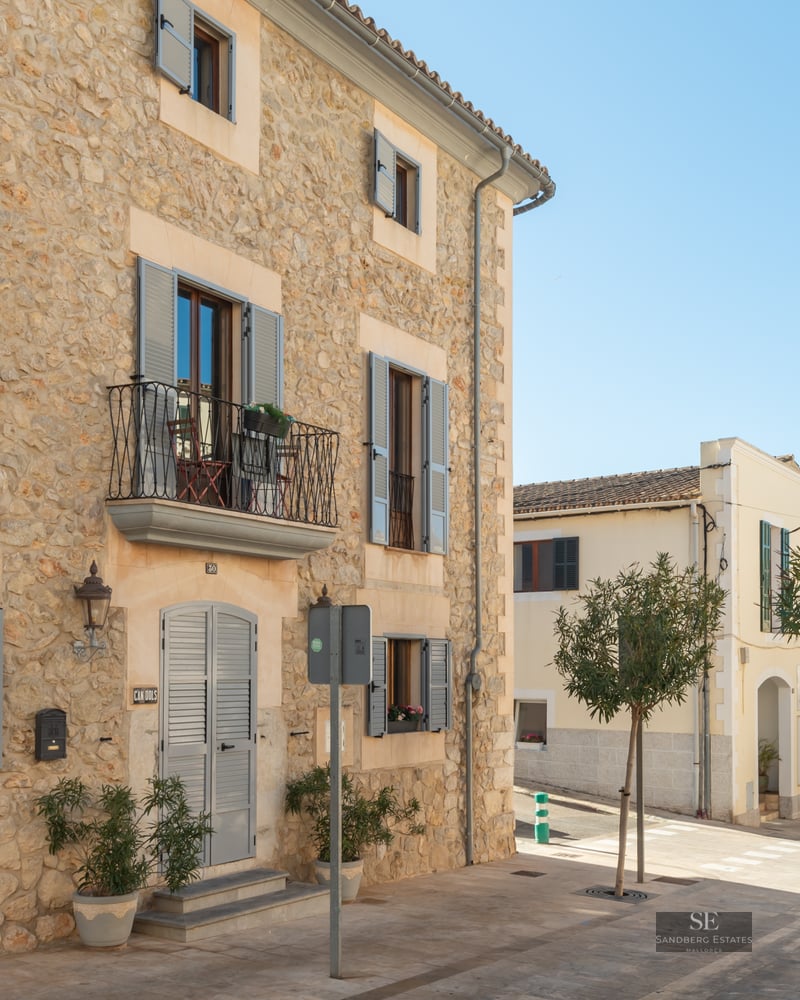 Traditional stone building with grey shutters and iron balconies on a sunny street.