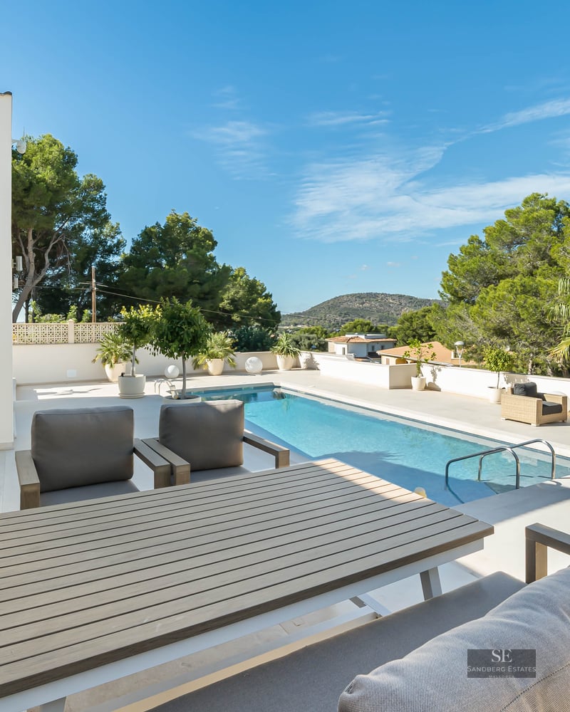 Grande terrasse ensoleillée avec une piscine rectangulaire, mobilier de salon élégant et cadre verdoyant.