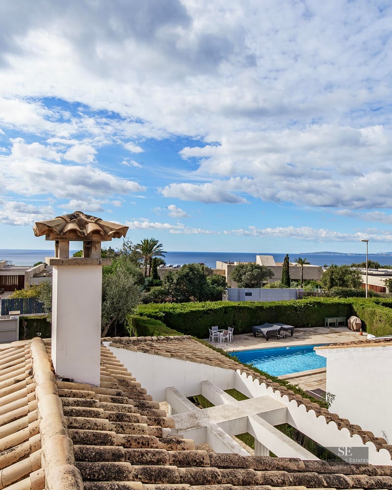 View from a tiled rooftop looking over a garden pool toward the Mediterranean Sea under a cloudy sky.