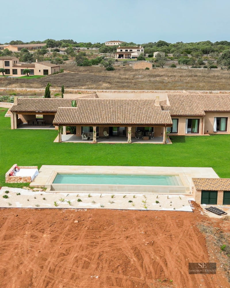 Bird's eye view of a luxury villa with terracotta roof, rectangular swimming pool, and large green lawn.