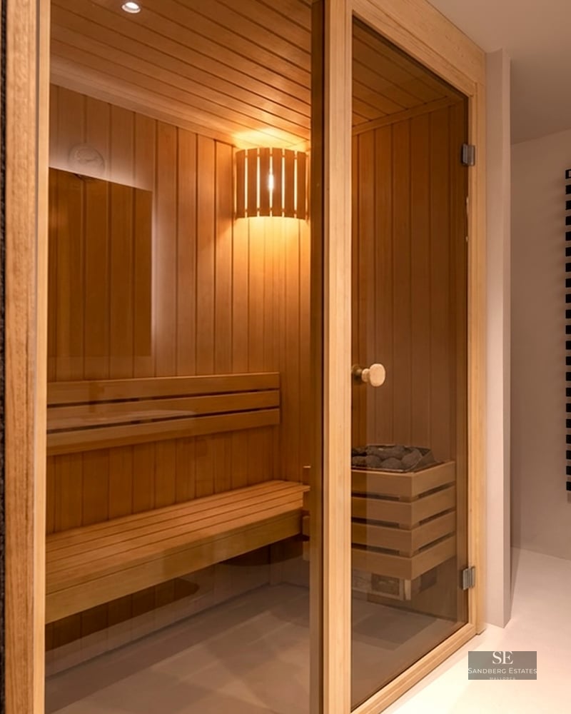 Sauna en bois clair avec porte vitrée, bancs à plusieurs niveaux et éclairage intérieur chaleureux.