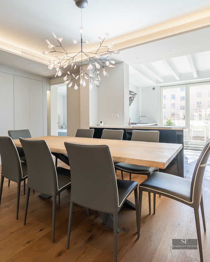 Modern dining room with a large light wood table, eight charcoal chairs, and a branch-style chandelier.