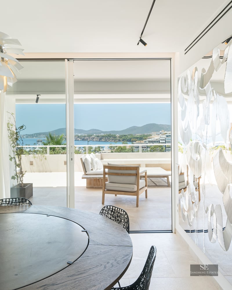 Luxury dining room featuring a round table, designer pendant light, and floor-to-ceiling windows overlooking a sea bay.