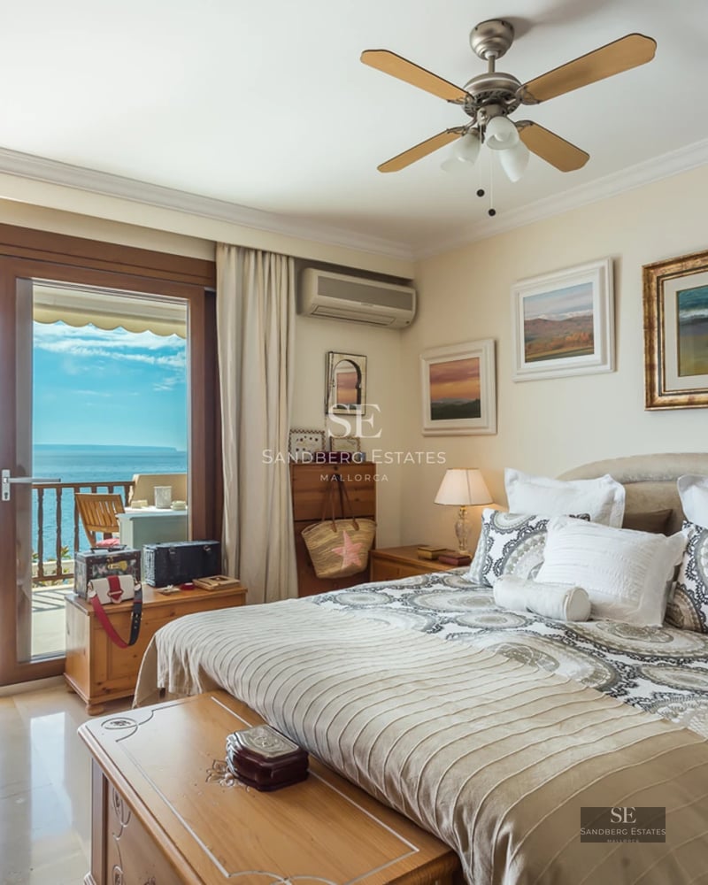 A bright master bedroom with patterned bedding and sliding glass doors opening onto a balcony with an expansive sea view.