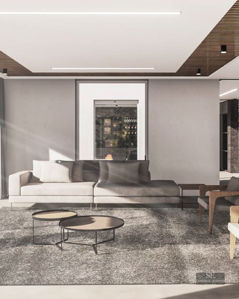 Minimalist living room with a grey sofa, wooden armchairs, and floor-to-ceiling windows showing a bright outdoor area.