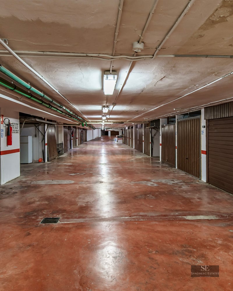 Underground garage hallway with red concrete floor and individual brown garage doors on both sides.