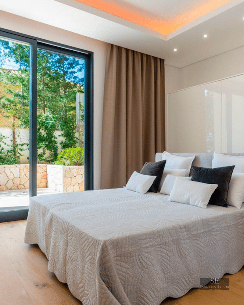 Bright bedroom featuring a large bed, wooden floors, and a sliding glass door opening to a private garden patio.