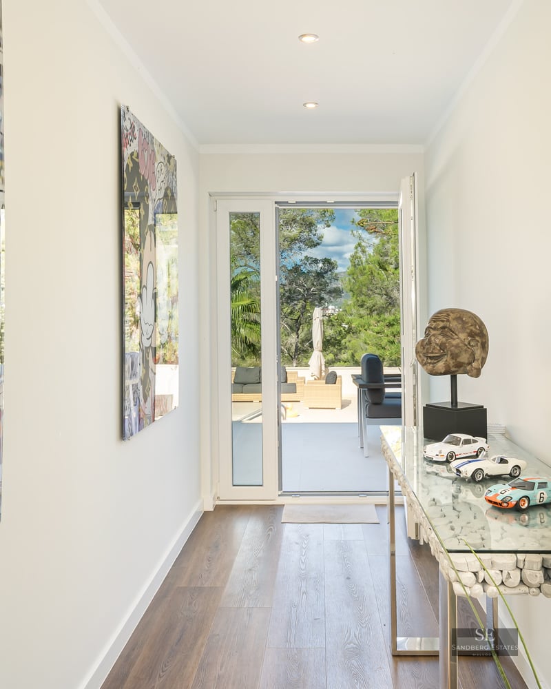 Couloir moderne lumineux avec du pop art vibrant, une console en verre et une porte ouverte sur une terrasse arborée.