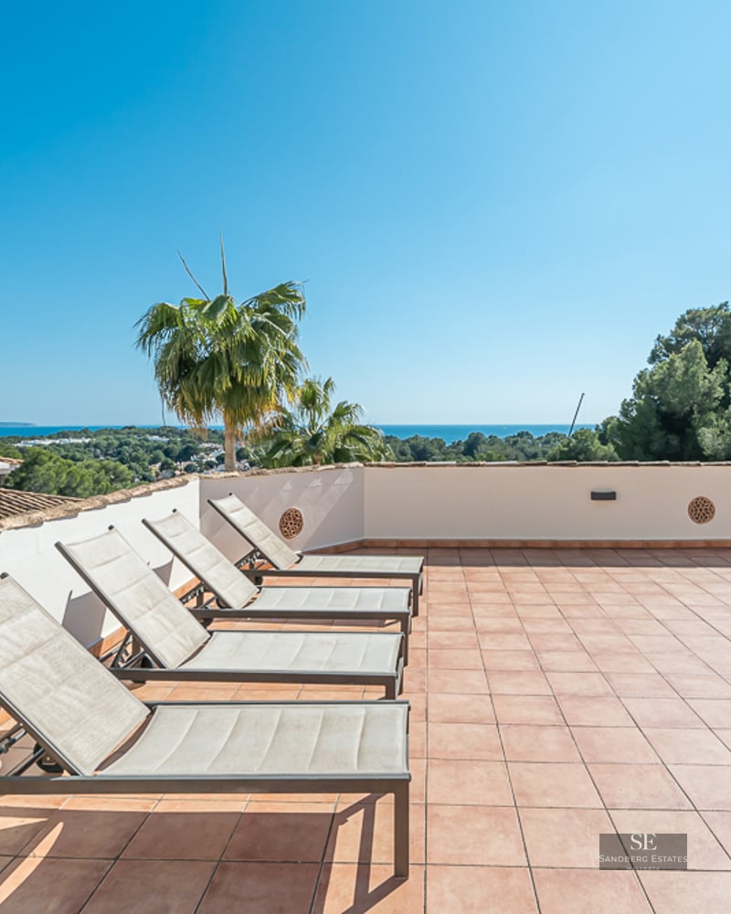 Grande terrasse en terre cuite avec quatre chaises longues et vue panoramique sur la mer sous un ciel bleu.