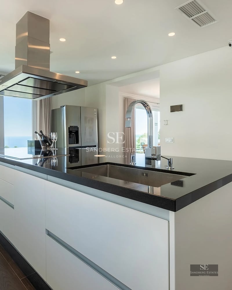 Sleek kitchen island with black countertop, stainless steel appliances, and a stunning ocean view through a large window.