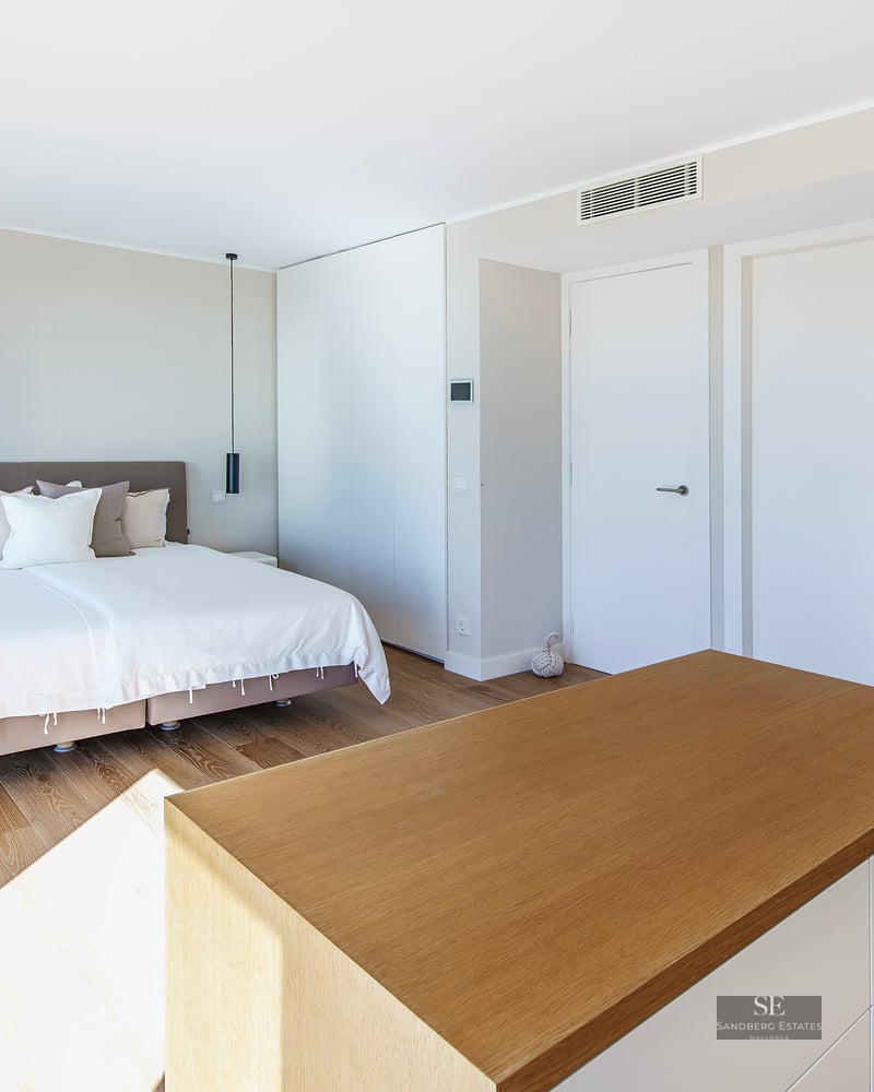 Modern bedroom with a large bed, light wood floors, and natural sunlight casting linear shadows.