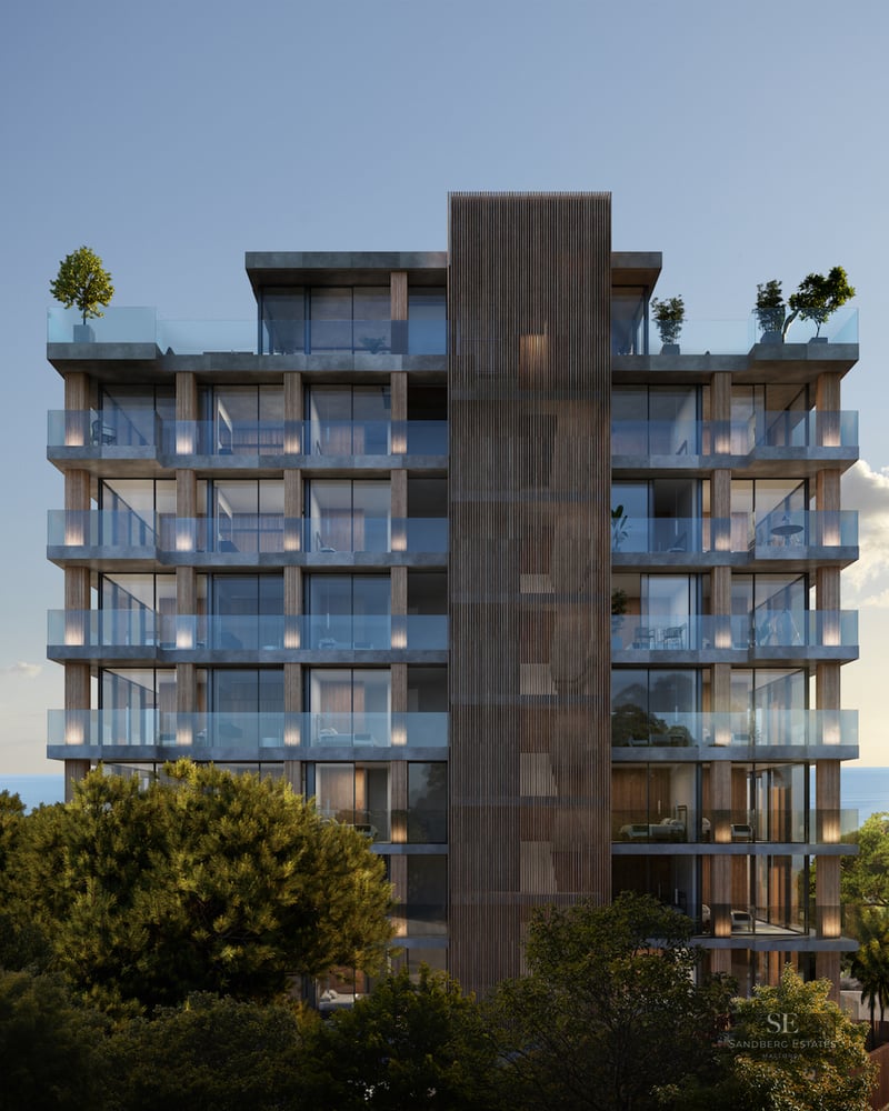 Modern multi-story building with glass balconies and wood accents surrounded by trees and sea views.