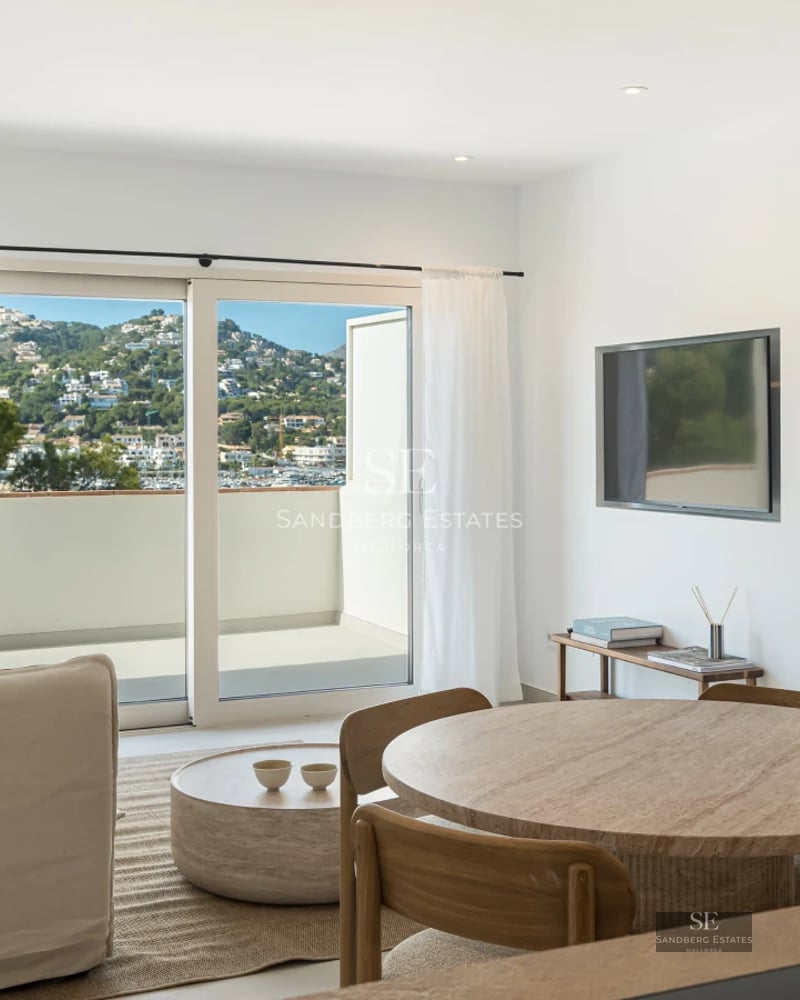 Spacious living room featuring expansive windows, designer sofas, a fireplace, and panoramic sea views. Natural lighting and hardwood floors.