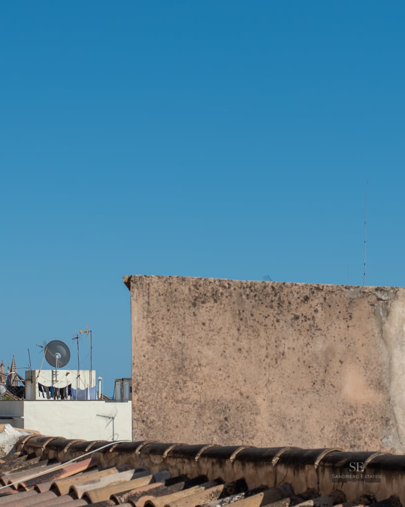 View from a tiled rooftop overlooking a historic Mediterranean city with a large Gothic cathedral under a clear blue sky.