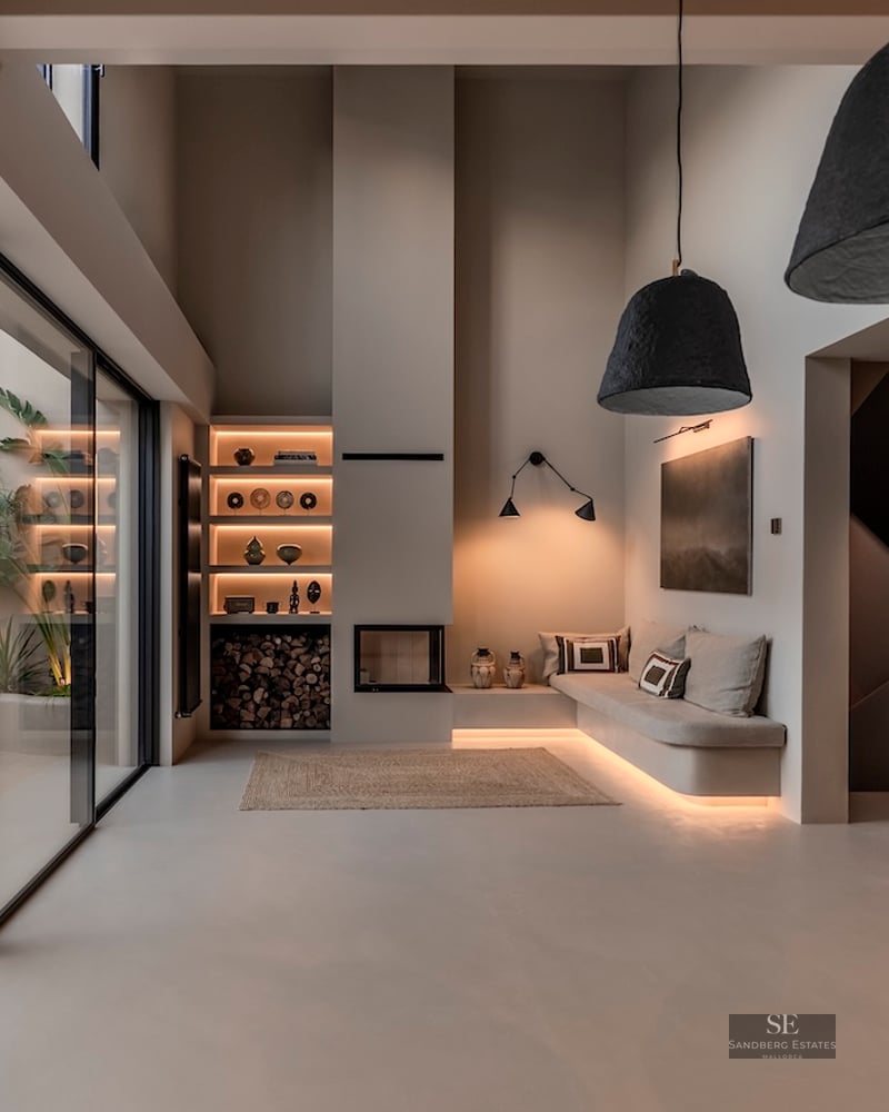 Salon minimaliste avec de hauts plafonds, un canapé intégré, une cheminée et de grandes baies vitrées sur un patio tropical.