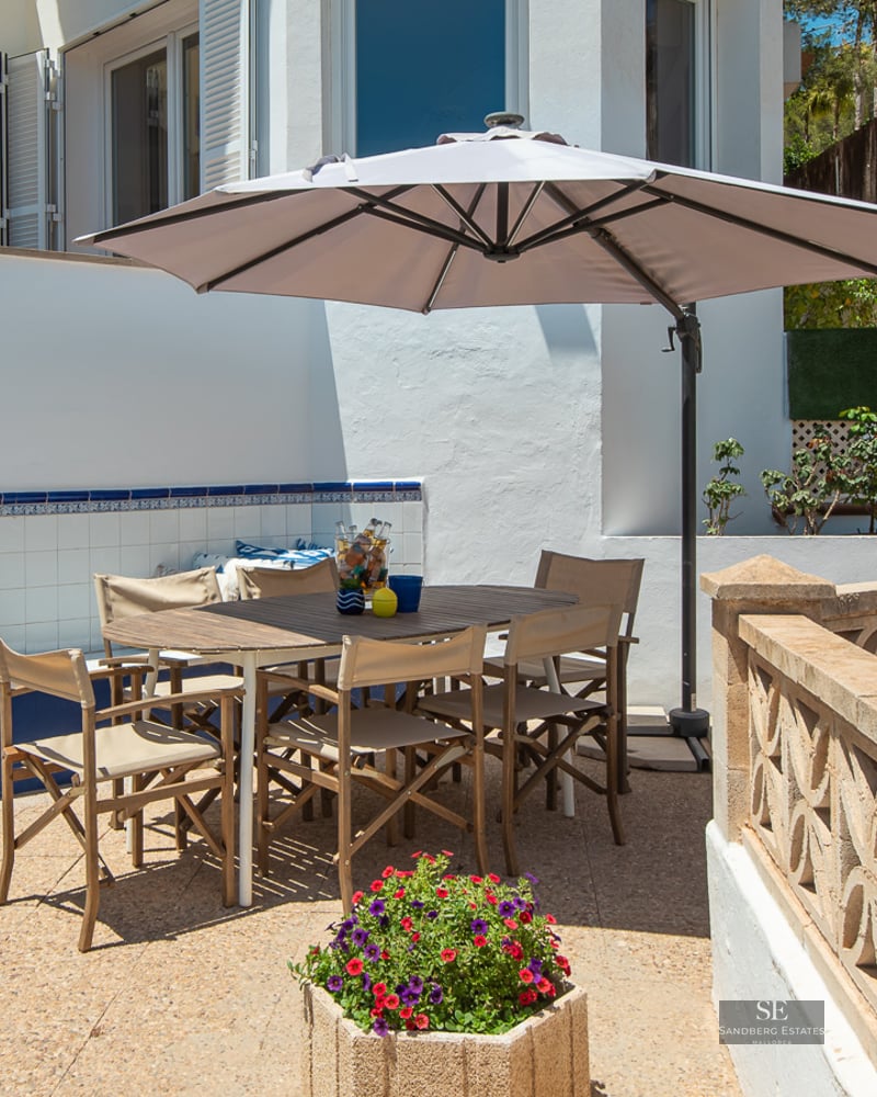 Sunny terrace featuring a wooden table, umbrella, blue tiled bench, and decorative stone balustrade.