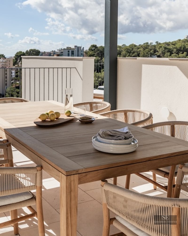 Modern outdoor dining area on a terrace featuring a wooden table, woven chairs, and a panoramic sea view.