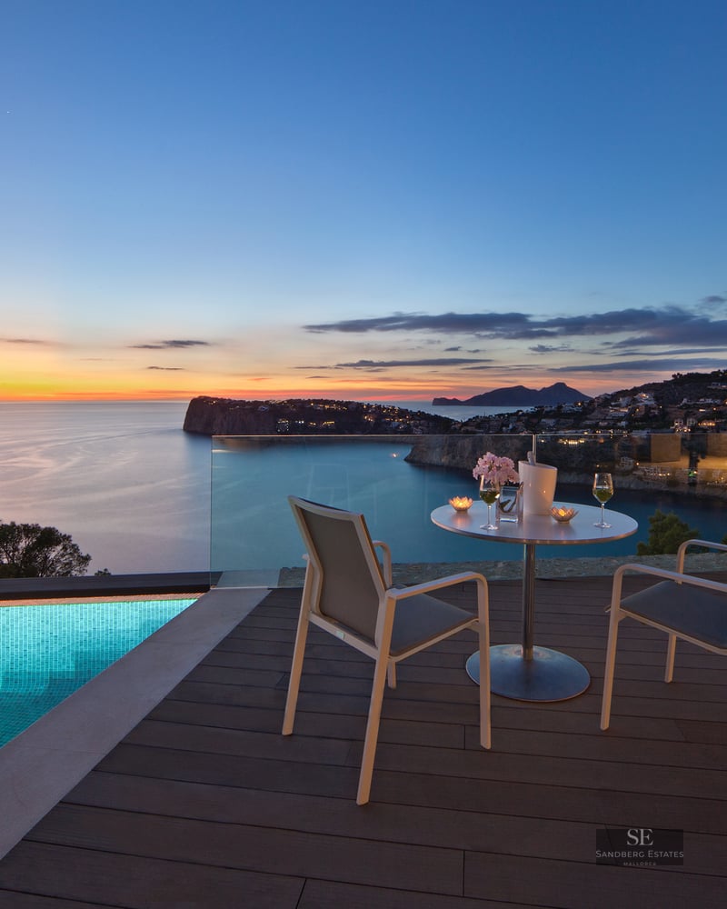 Luxury terrace with infinity pool, table for two, and panoramic sea view at sunset.