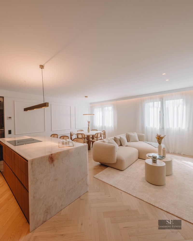 Bright open-plan living room with a large marble kitchen island, curved beige sofa, and herringbone wood floors.