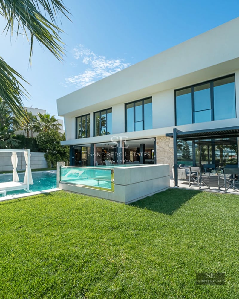 Spacious living room with panoramic windows, ocean view, light wood floors, fireplace, and modern furniture in neutral tones.