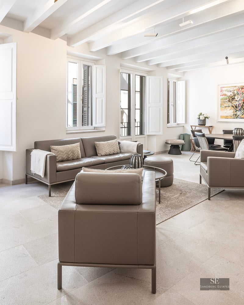 Spacious living room with taupe leather sofas, white beamed ceiling, and large windows with shutters.