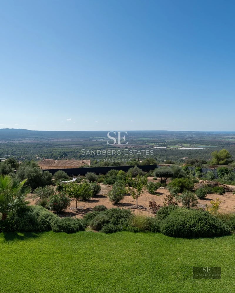 View of infinity pool with loungers and lush garden. Modern architecture with large windows and clear sky.