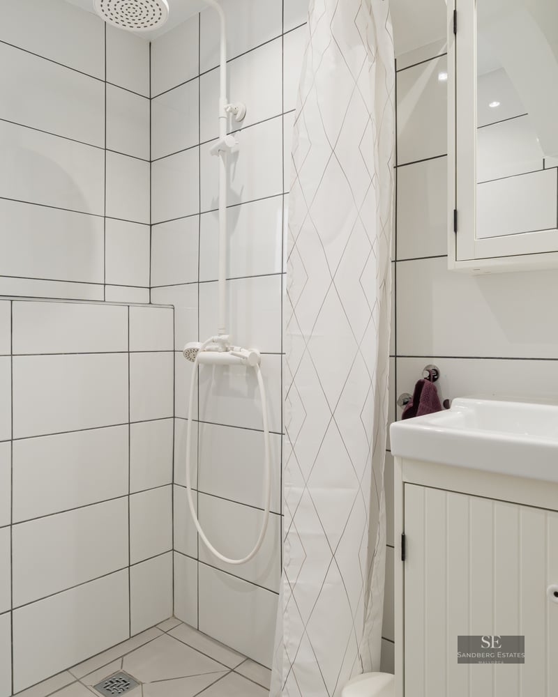 White tiled bathroom with a sink, toilet, and shower area separated by a white curtain.