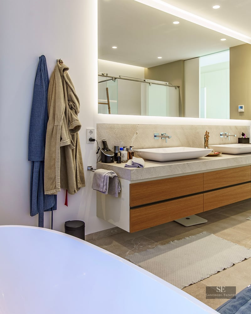 Salle de bain de luxe avec double vasque en bois, miroir rétroéclairé, douche en verre et baignoire îlot blanche.