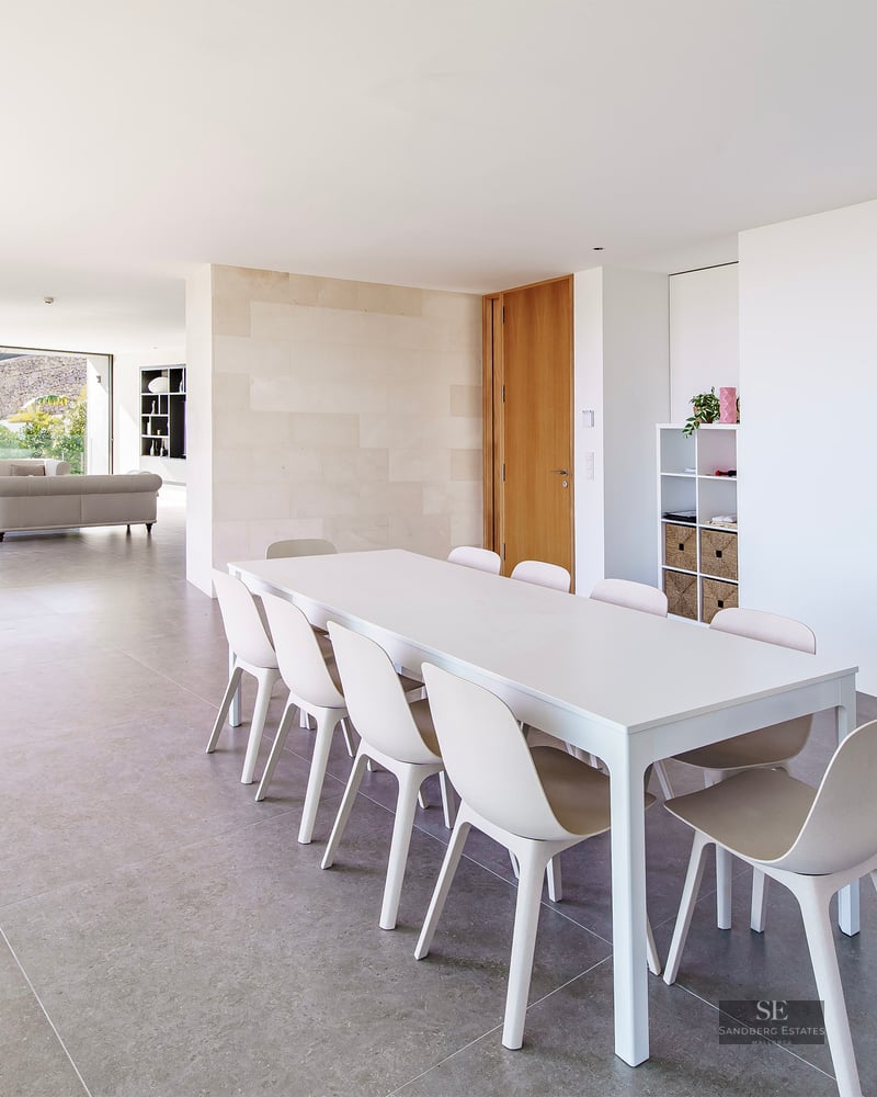 Bright minimalist dining room with white table and chairs, leading into a spacious living area with floor-to-ceiling windows.