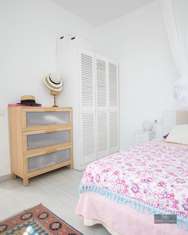 Bedroom with pink patterned bedspread, white canopy, light wood dresser, and white louvered wardrobe on tiled floor.